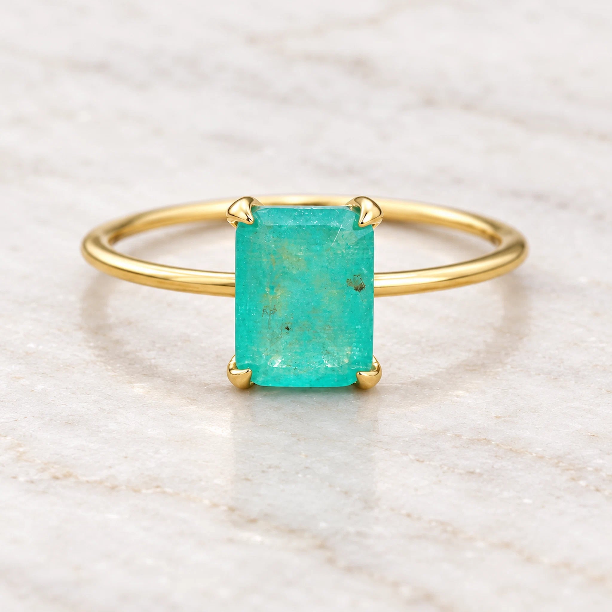 Gold ring with a green blue natural tourmaline gemstone on a beige marble background