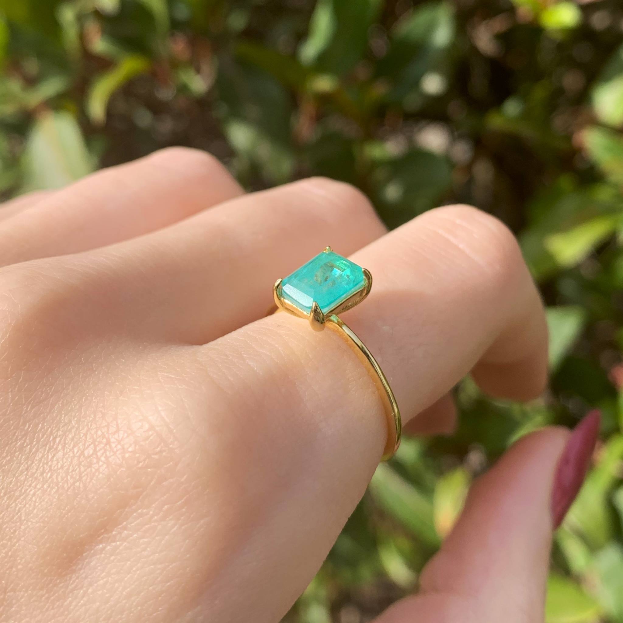 Gold ring with a green natural tourmaline gemstone on a hand against a blurred green background