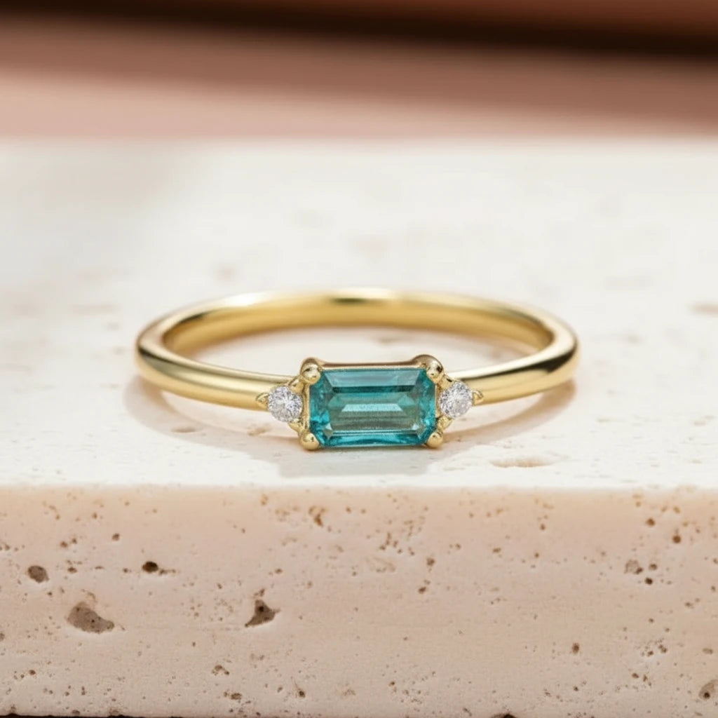 Gold ring with a green tourmaline gemstone on a textured surface with dried plants.