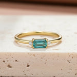 Gold ring with a green tourmaline gemstone on a textured surface with dried plants.