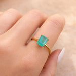 Gold ring with a green blue natural tourmaline gemstone on a finger against a neutral background