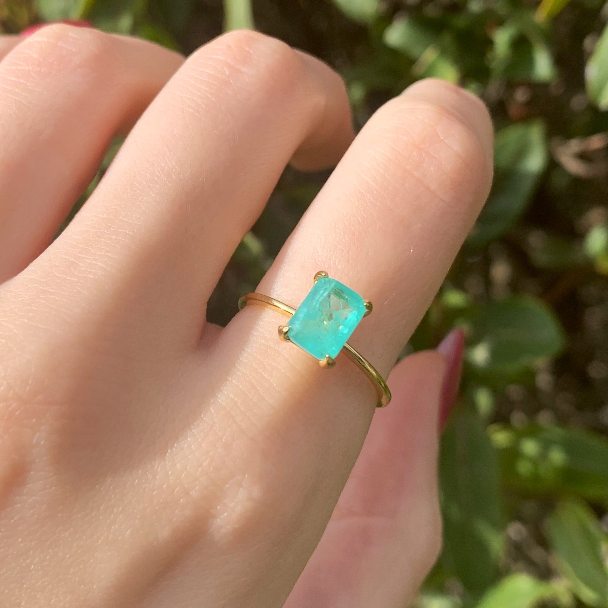 Gold ring with a green blue tourmaline gemstone on a finger against a blurred green background