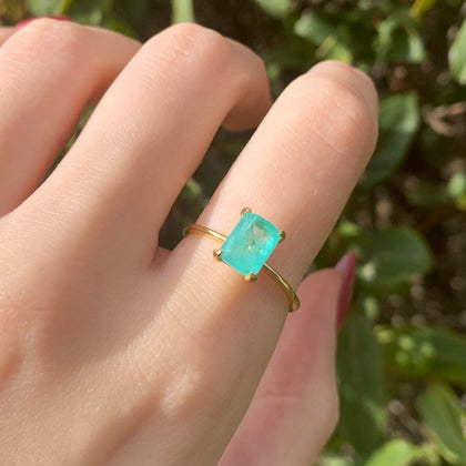 Gold ring with a green blue tourmaline gemstone on a finger against a blurred green background