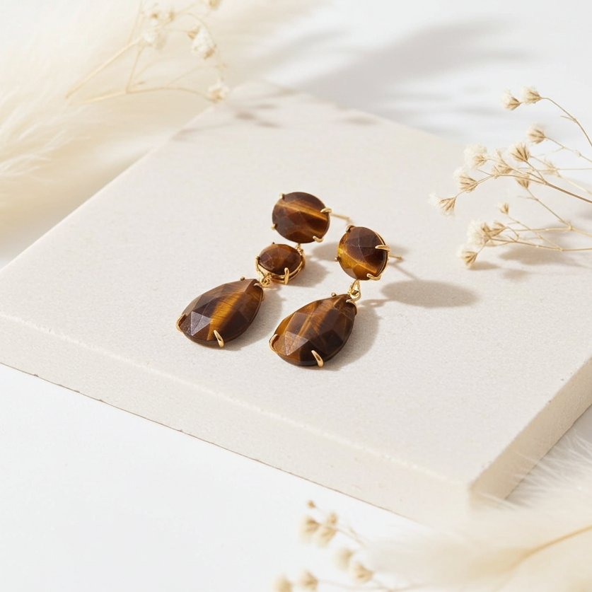 Pair of indie and harper gold tiger eye earrings on a white surface with dried flowers 
