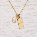 gold U initial and aquarius zodiac necklace on fine gold chain against a light wooden background