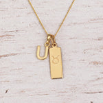 Gold U Initial and Taurus Necklace on a fine gold chain against a light wooden background