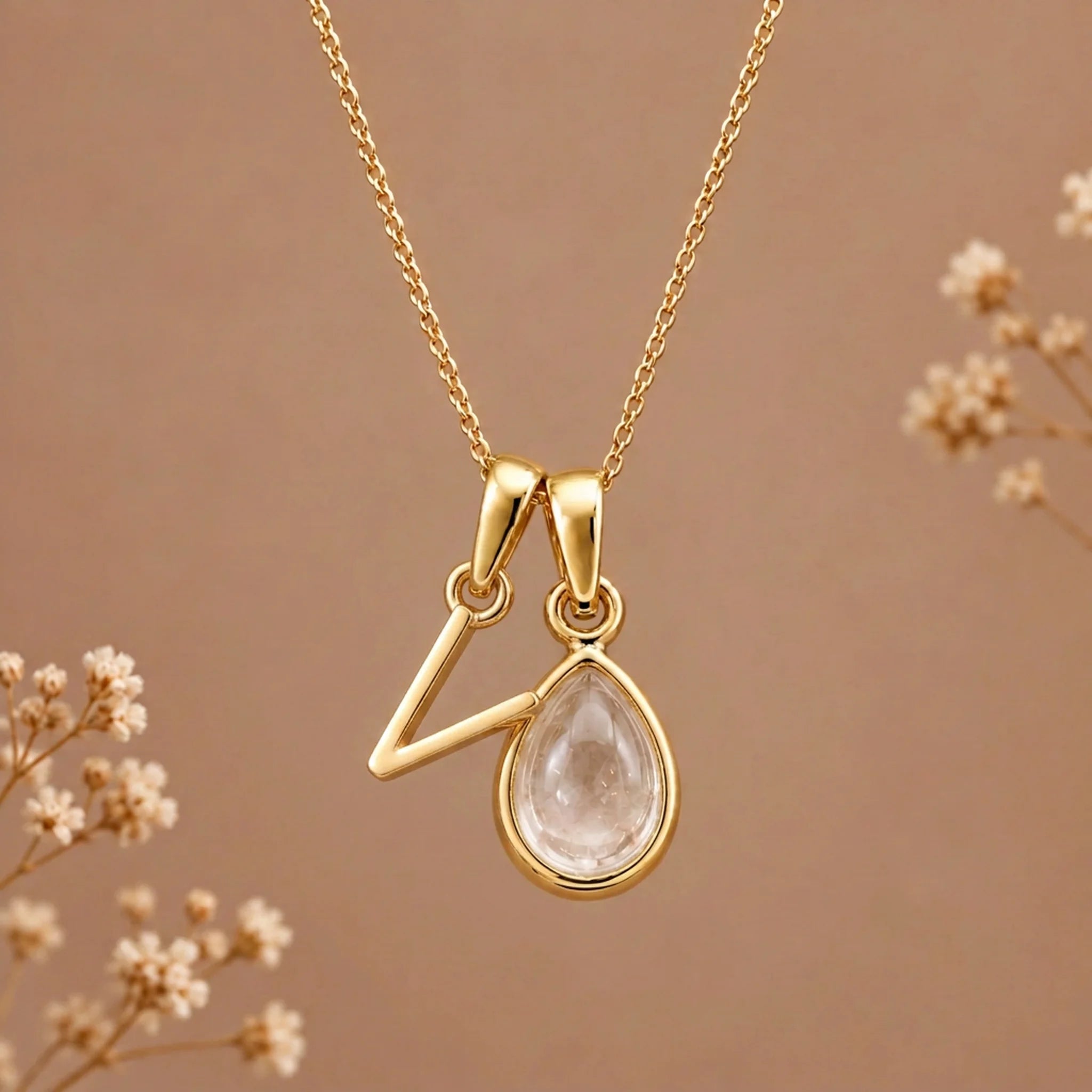 Gold initial V necklace with an April clear quartz teardrop on brown with dried flowers
