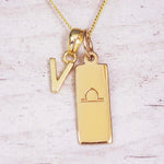 Gold initial and Libra zodiac necklace with a letter V charm and engraved bar pendant on whitewashed wood