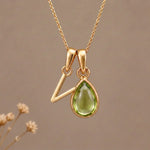 Gold Initial V Pendant and August birthstone Natural Peridot Necklace against a warm background
