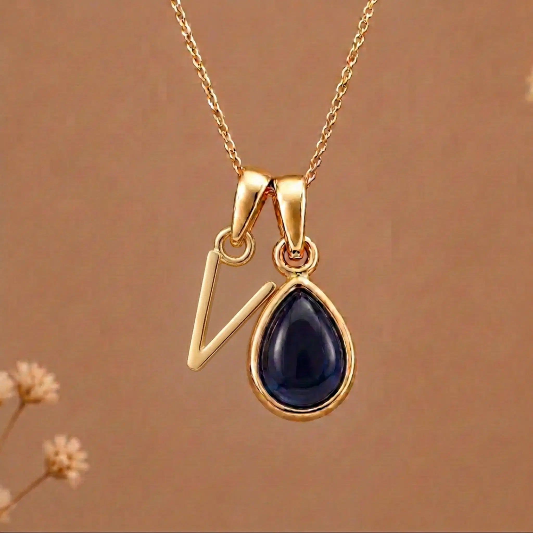 Gold Initial V Pendant and September birthstone Natural Sapphire Necklace against a warm background