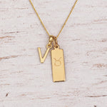 Gold V Initial and Taurus Necklace on a fine gold chain against a light wooden background