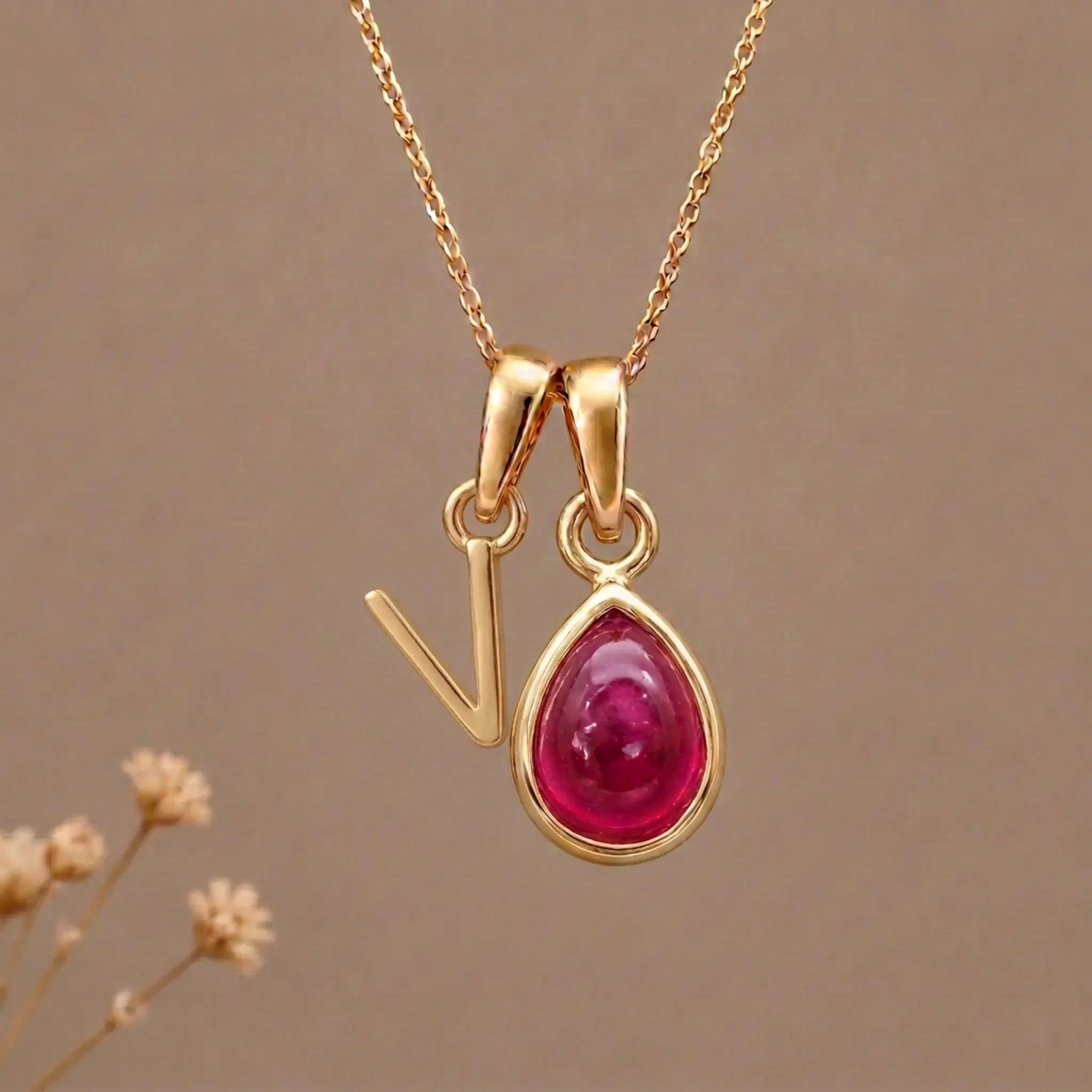 Gold Initial V Pendant and July birthstone Natural Ruby Necklace against a warm background