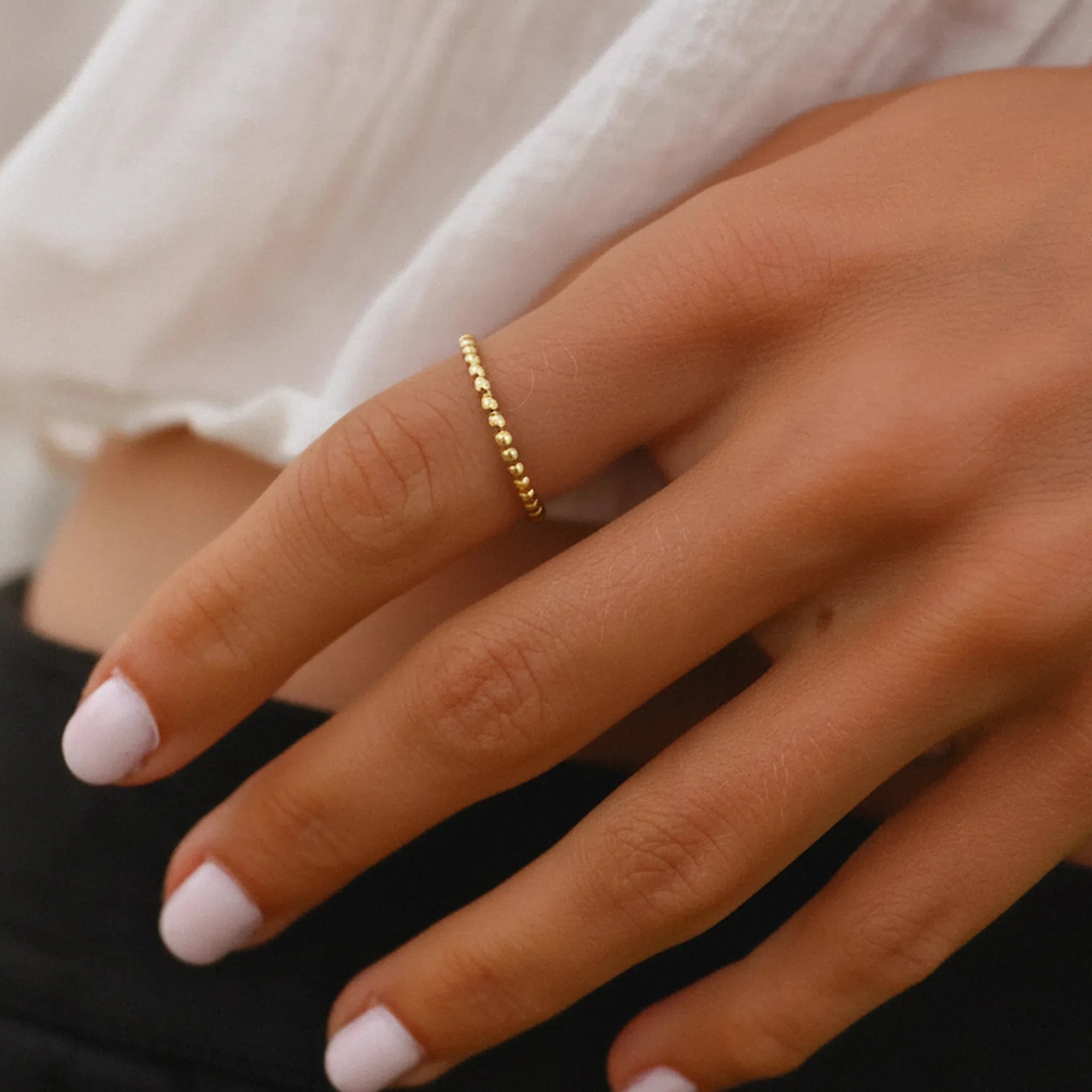 Close-up of a hand wearing a dainty gold vermeil stacker ring with a blurred background