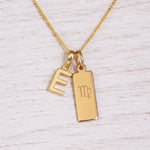 Gold Virgo initial necklace with a letter E pendant and zodiac bar on whitewashed wood