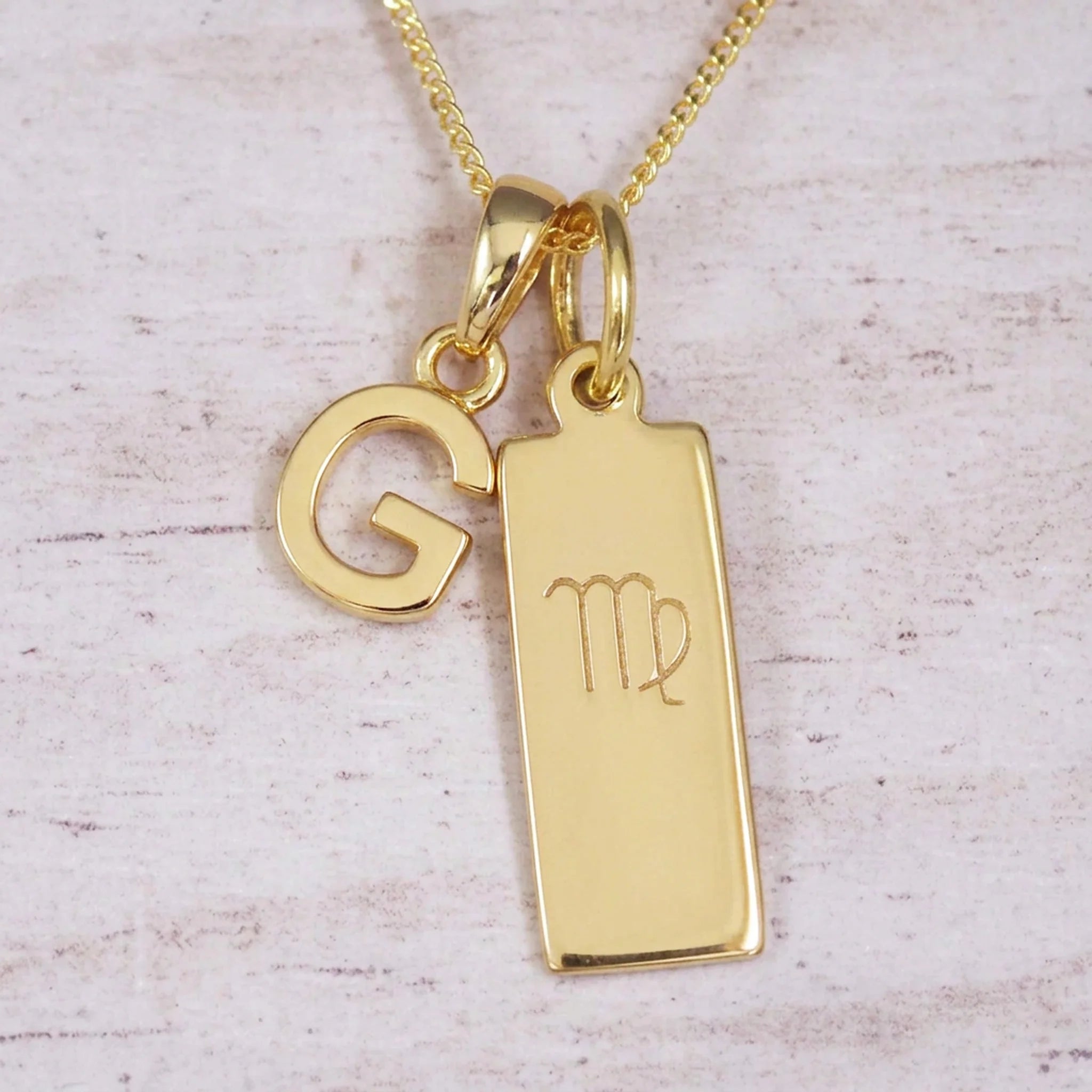 Gold Virgo initial necklace with a letter G pendant and zodiac bar on whitewashed wood