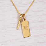 Gold Virgo initial necklace with a letter I pendant and zodiac bar on whitewashed wood