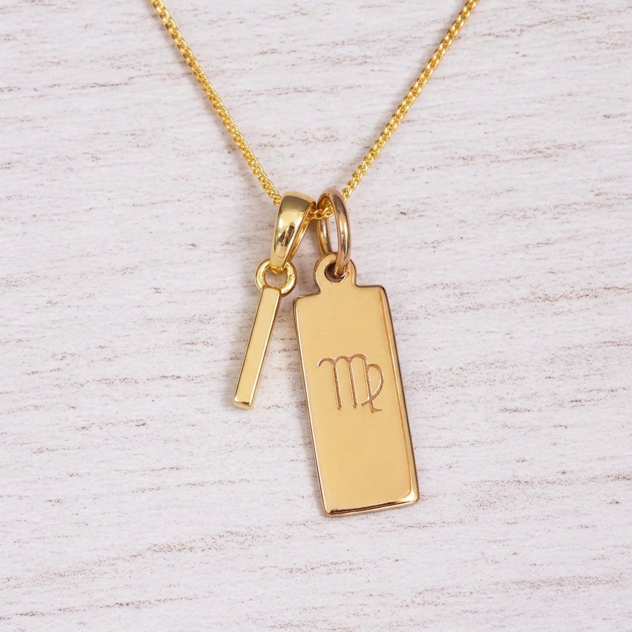 Gold Virgo initial necklace with a letter I pendant and zodiac bar on whitewashed wood