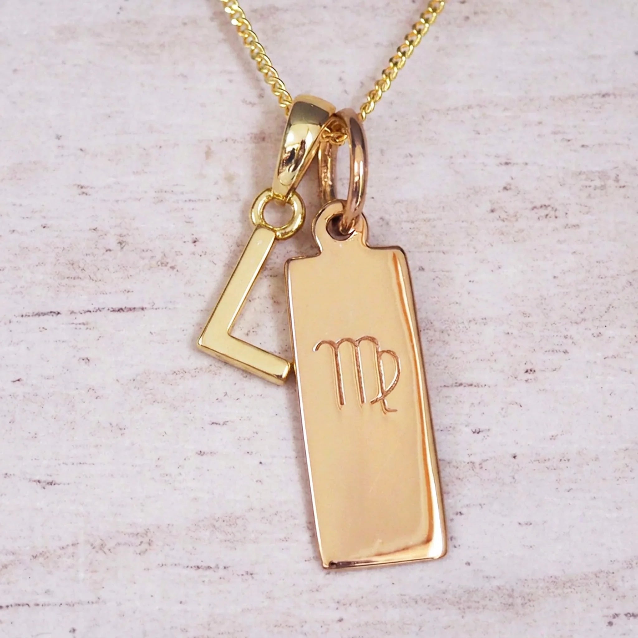 Gold Virgo initial necklace with a letter L pendant and zodiac bar on whitewashed wood