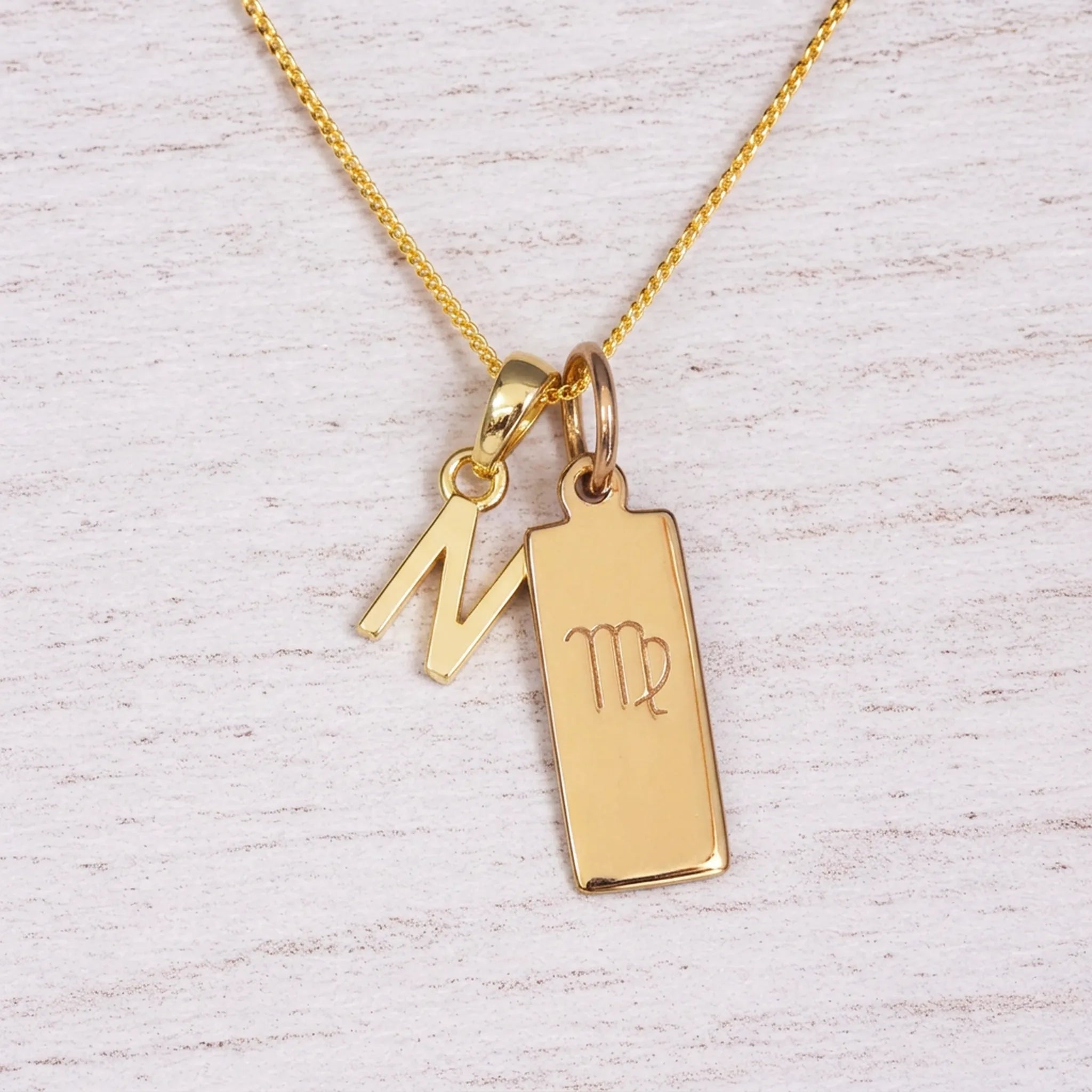 Gold Virgo initial necklace with a letter N pendant and zodiac bar on whitewashed wood