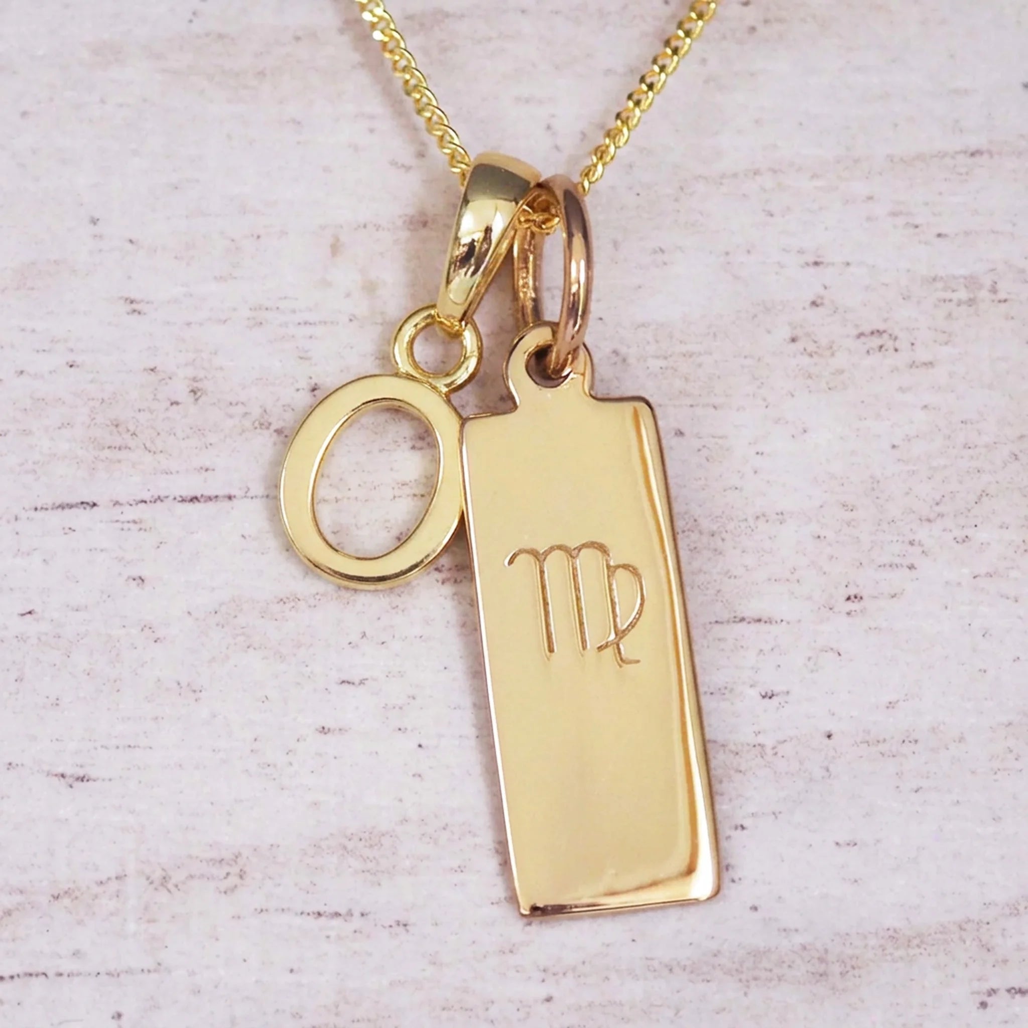 Gold Virgo initial necklace with a letter O pendant and zodiac bar on whitewashed wood