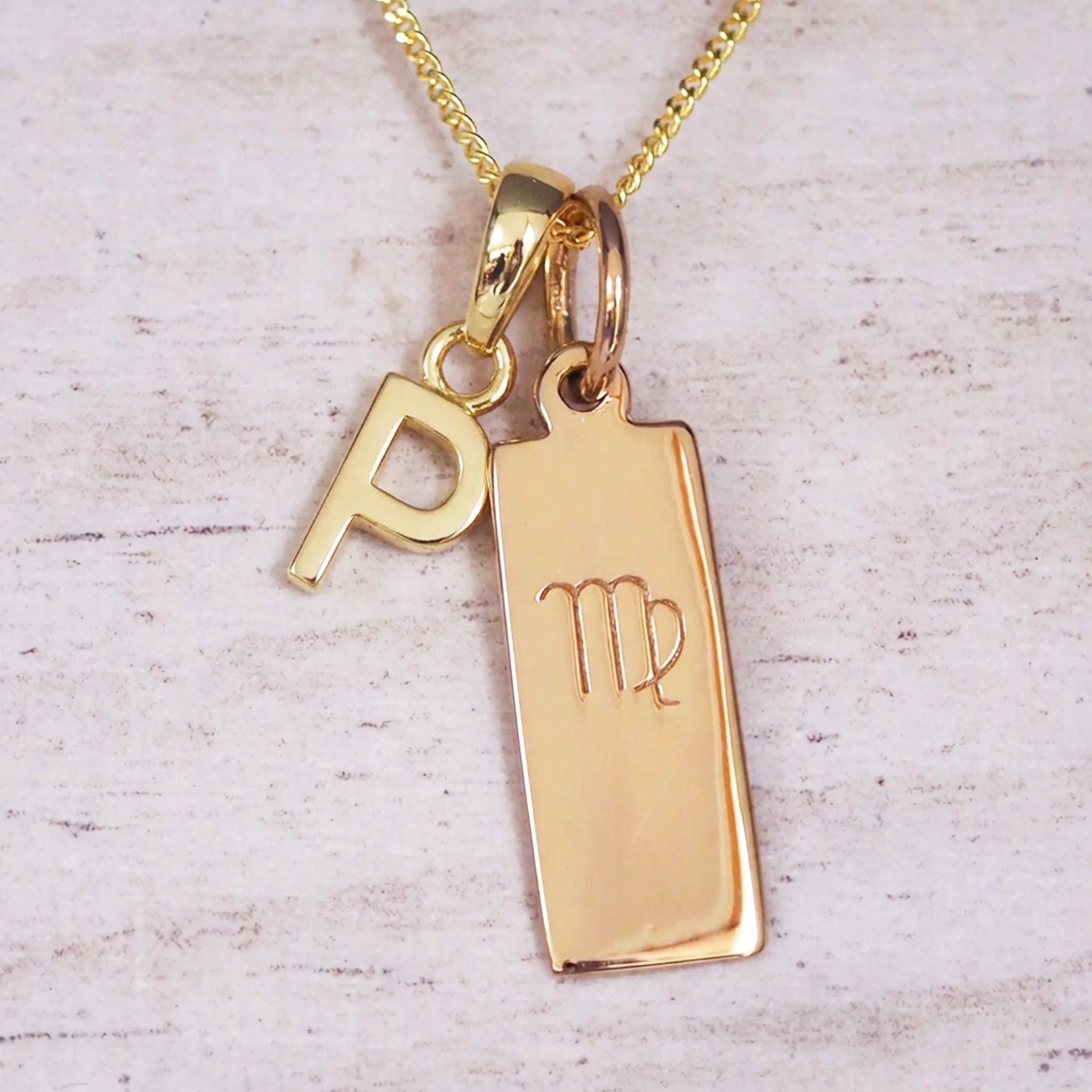 Gold Virgo initial necklace with a letter P pendant and zodiac bar on whitewashed wood