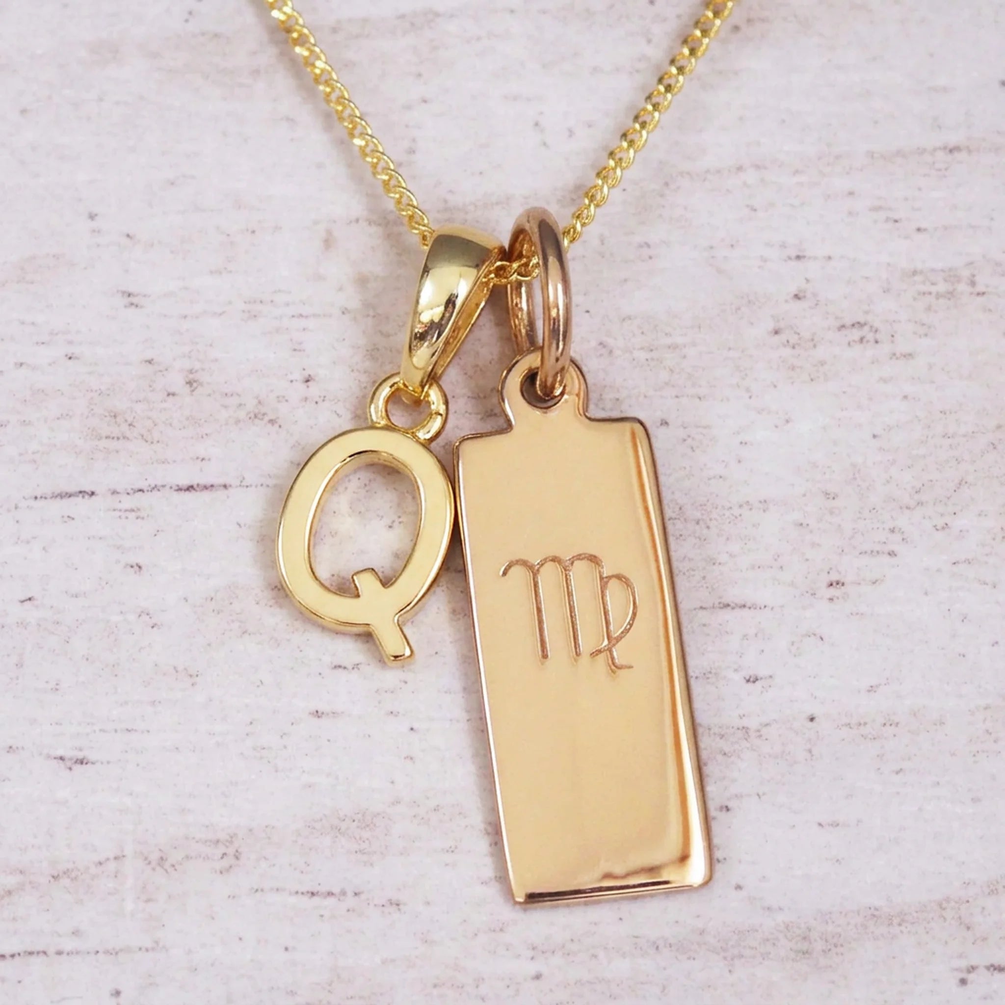 Gold Virgo initial necklace with a letter Q pendant and zodiac bar on whitewashed wood