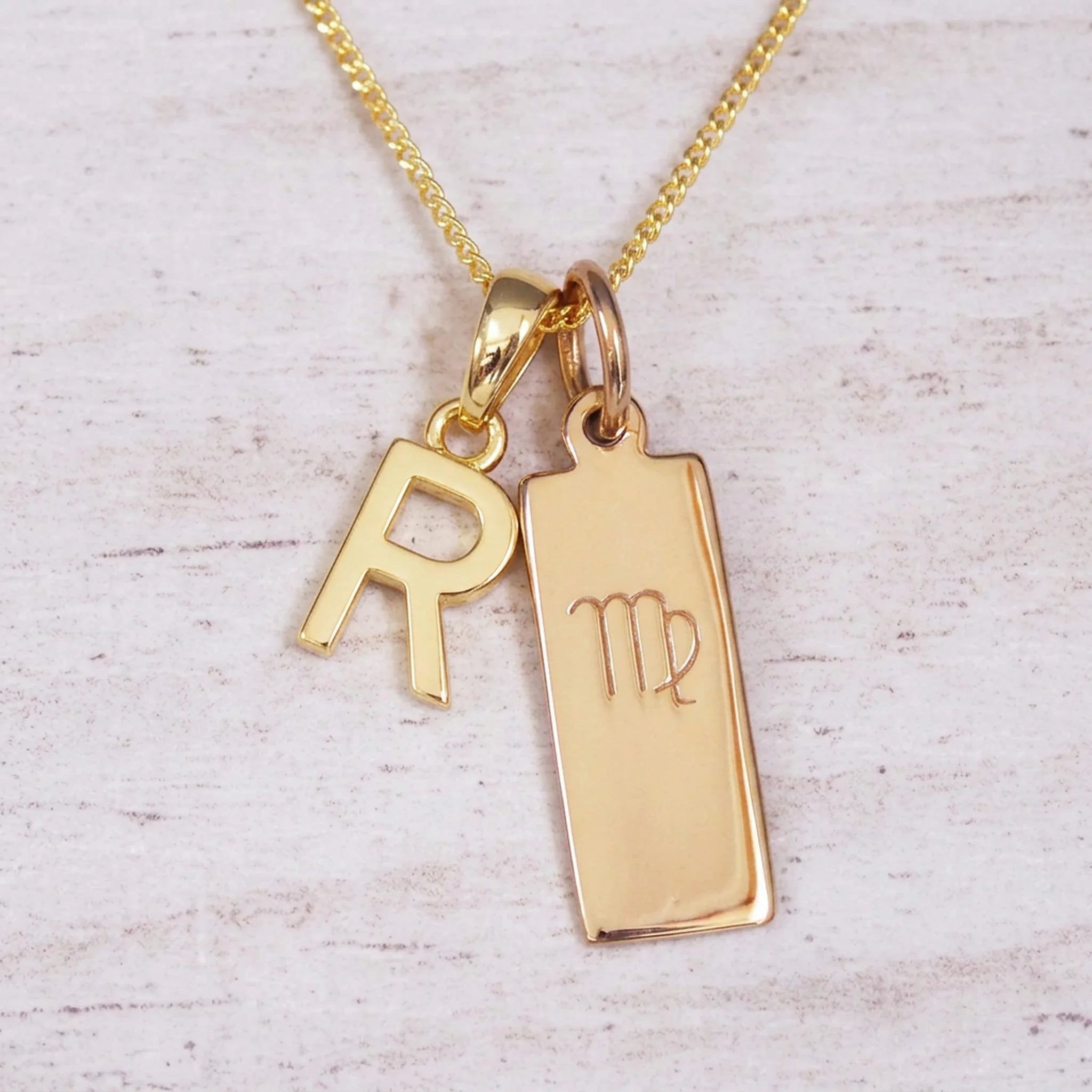 Gold Virgo initial necklace with a letter R pendant and zodiac bar on whitewashed wood