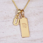 Gold Virgo initial necklace with a letter U pendant and zodiac bar on whitewashed wood