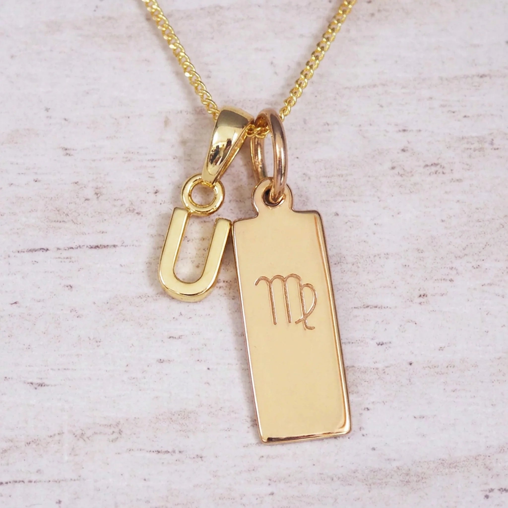 Gold Virgo initial necklace with a letter U pendant and zodiac bar on whitewashed wood