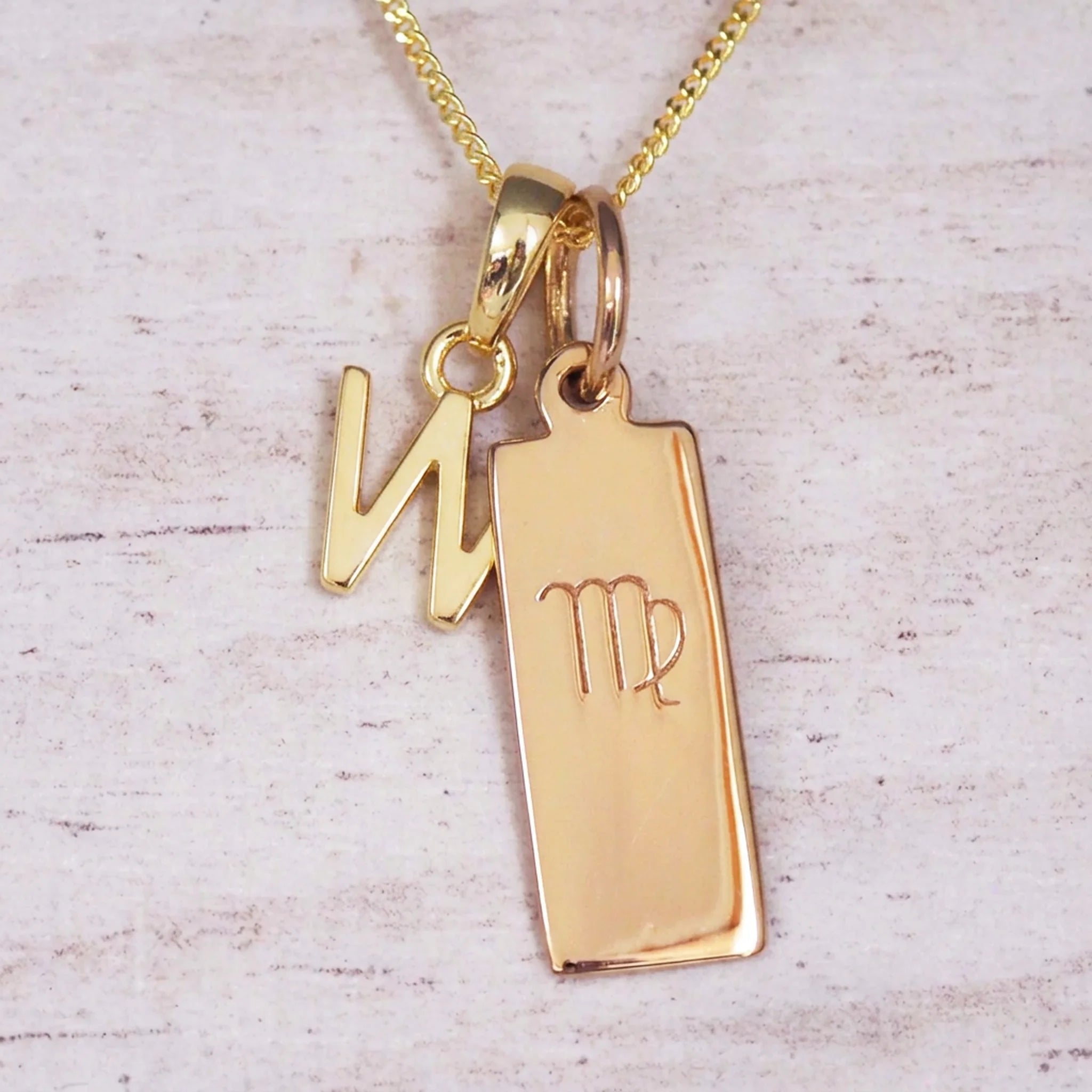 Gold Virgo initial necklace with a letter W pendant and zodiac bar on whitewashed wood