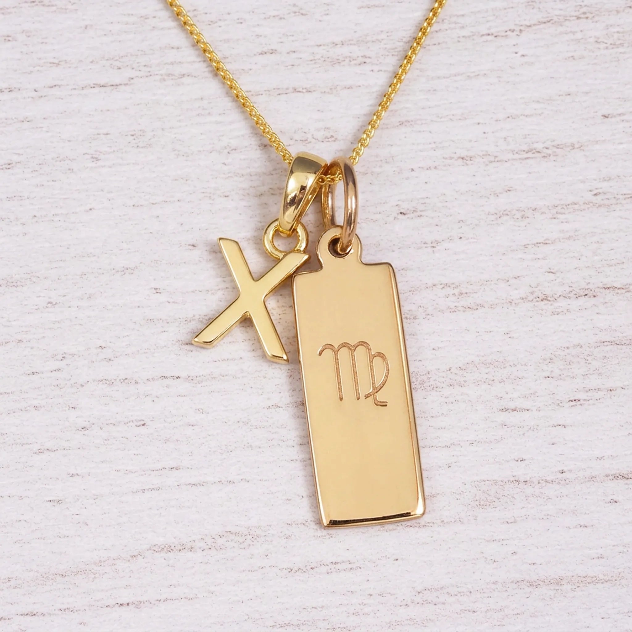 Gold Virgo initial necklace with a letter X pendant and zodiac bar on whitewashed wood