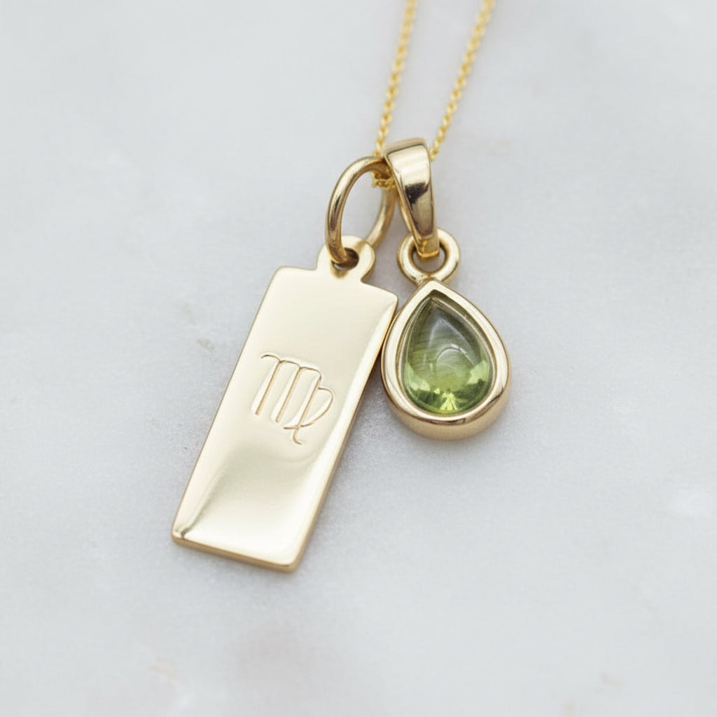 Gold necklace with virgo zodiac pendant and tear drop natural peridot pendant on a light stone surface
