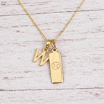 Gold Initial W Pendant and Cancer Zodiac Pendant Necklace on a fine gold chain against a light wooden background