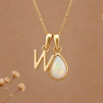 Gold Initial W Pendant and October birthstone Natural Opal Necklace against a warm background