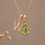 Gold Initial W Pendant and August birthstone Natural Peridot Necklace against a warm background