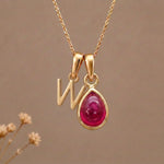 Gold Initial W Pendant and July birthstone Natural Ruby Necklace against a warm background