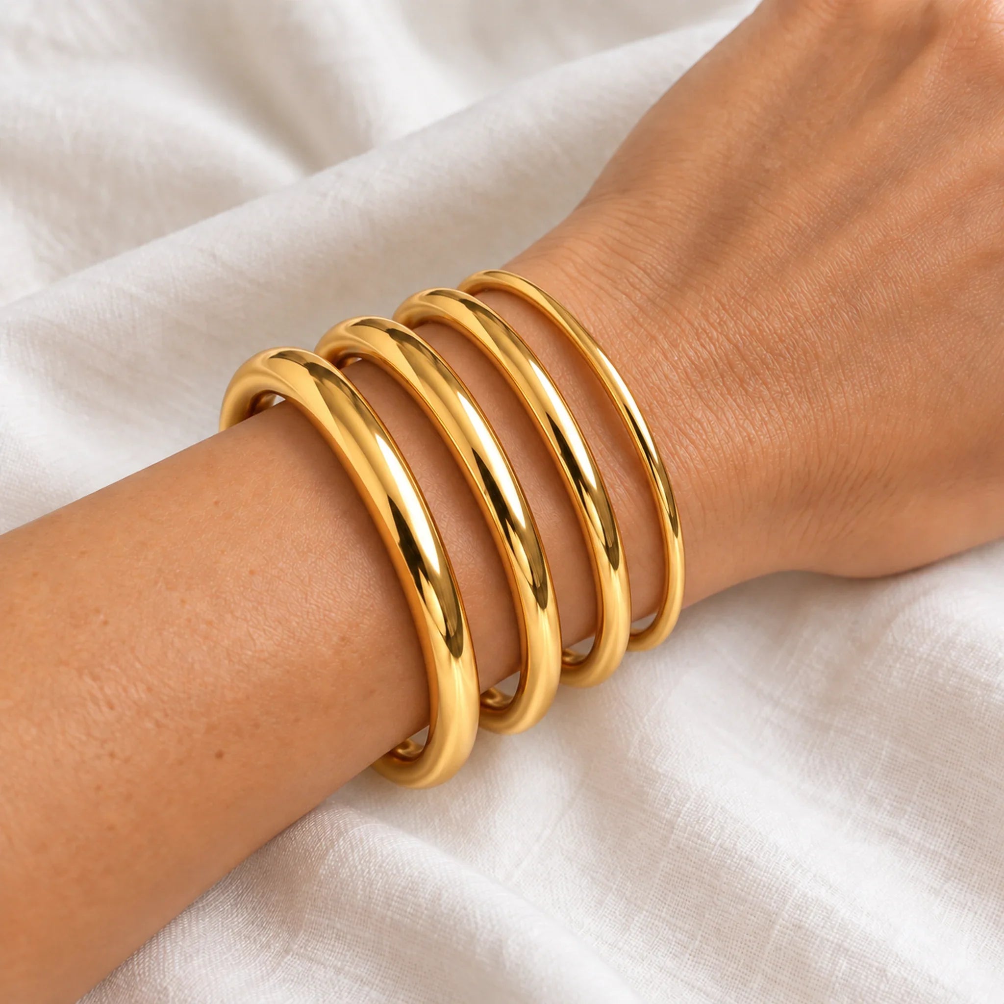 Four gold waterproof classic bangles worn together in 4, 6, 8 and 10 mm widths, 61 mm internal diameter