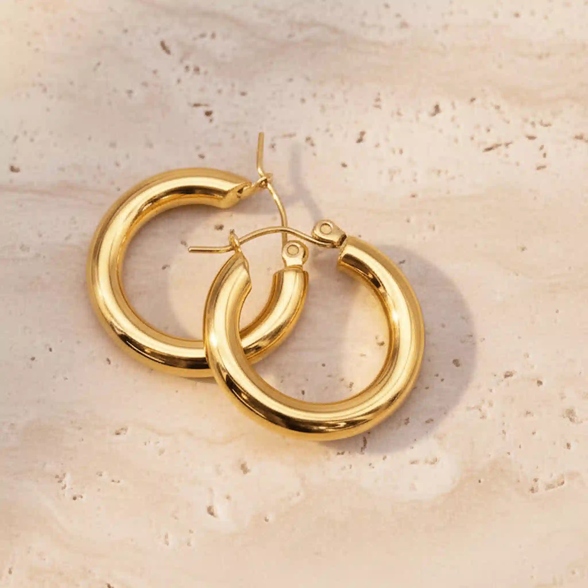 Gold waterproof hoop earrings on a beige stone surface