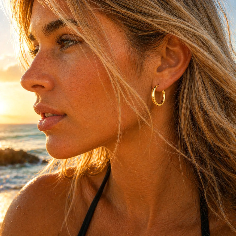 Woman wearing classic gold waterproof hoop earrings on a beach at sunset