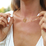 woman holding a gold waterproof necklace with starburst compass charm pendant in stainless steel