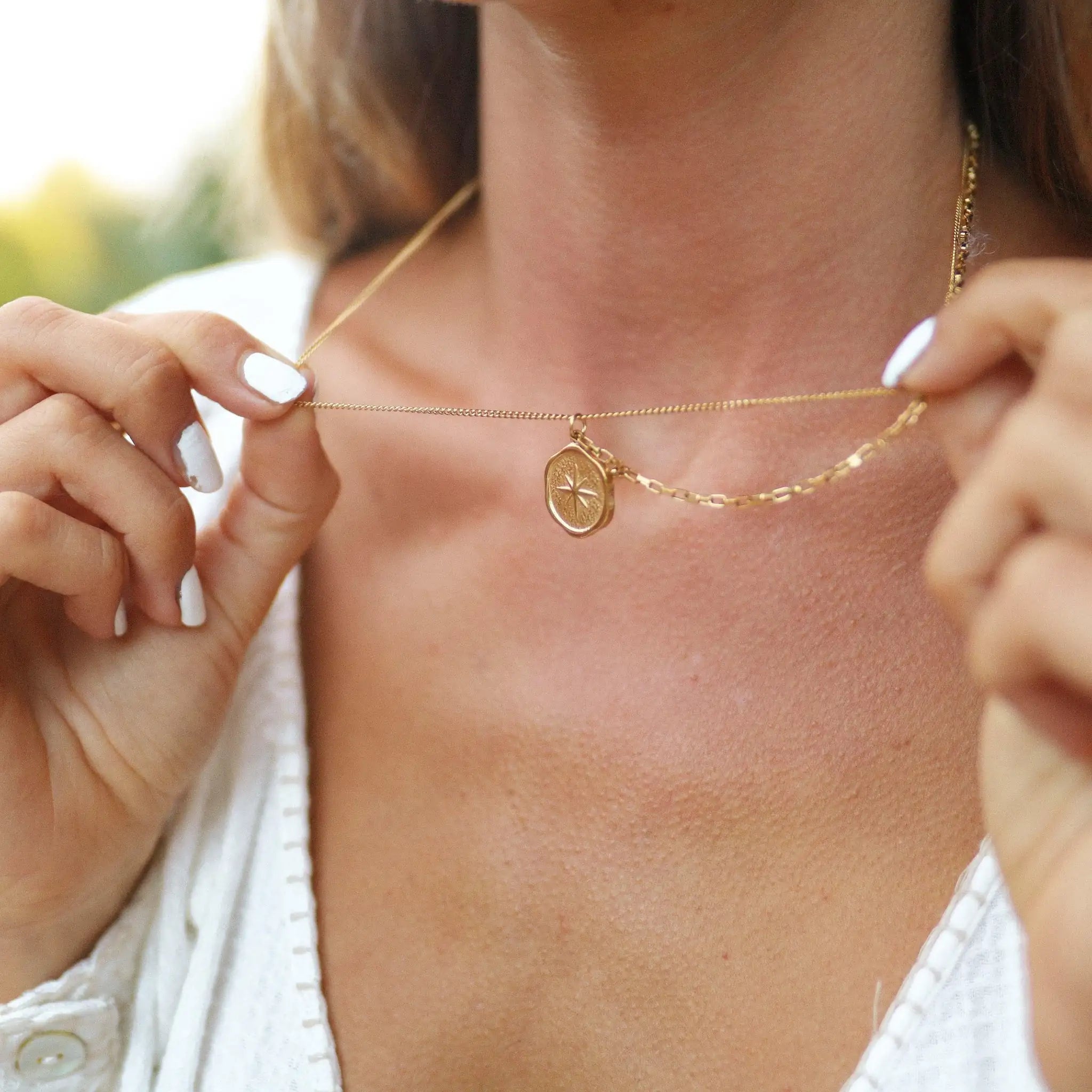 woman holding a gold waterproof necklace with starburst compass charm pendant in stainless steel