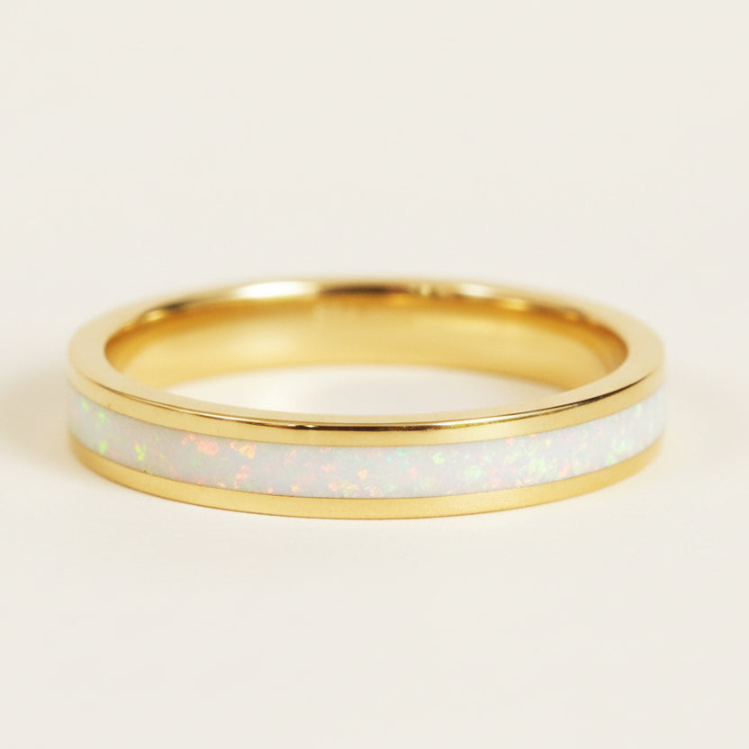 Gold ring with a white opal inlay on a textured beige background