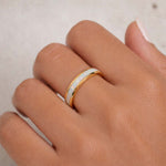 Gold ring with a white opal stone on a person's finger against a neutral background