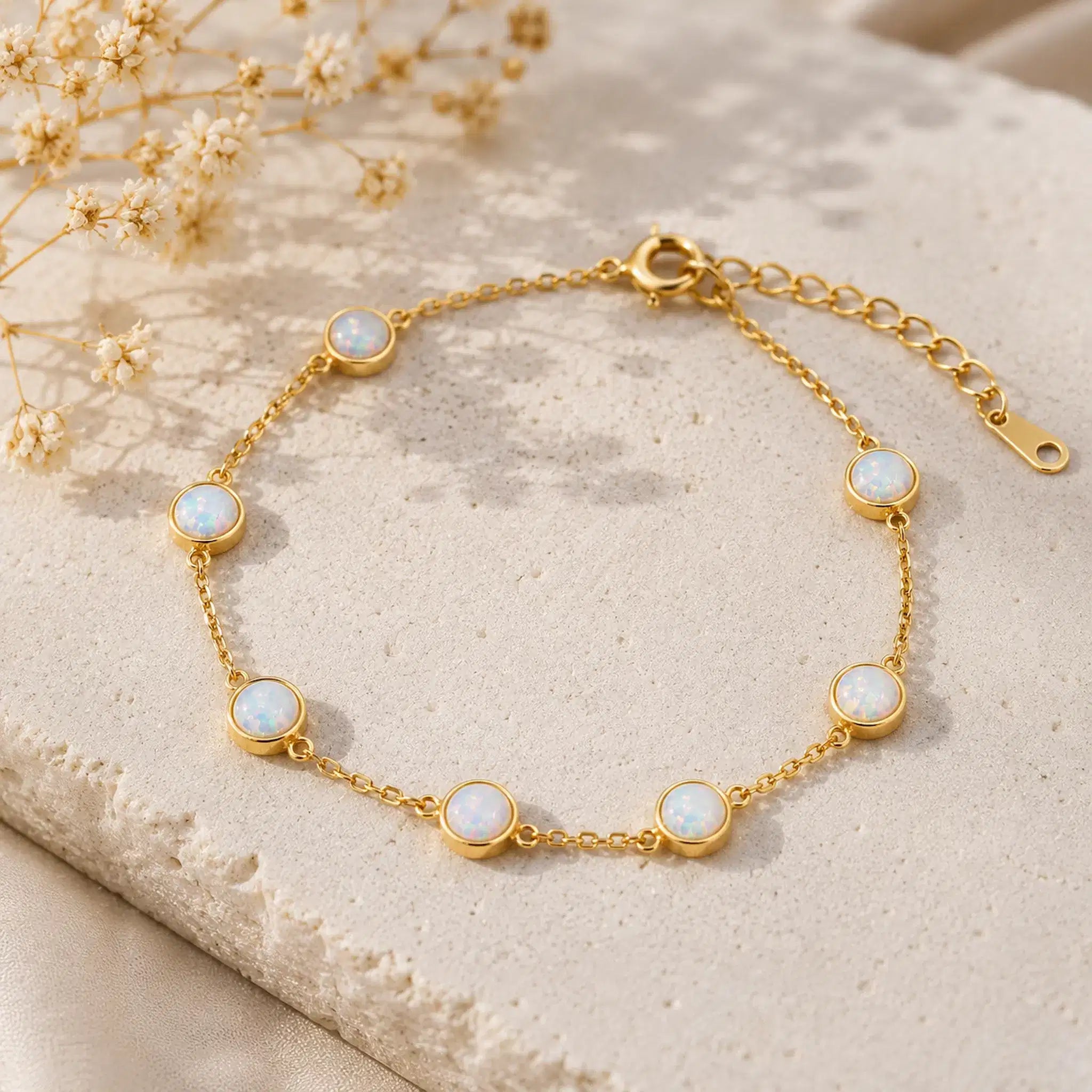 dainty gold chain bracelet with bezel set white opals on a light stone surface