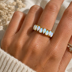 A gold band ring featuring a row of teardrop-shaped white opal stones with blue iridescent flashes, worn on a hand.