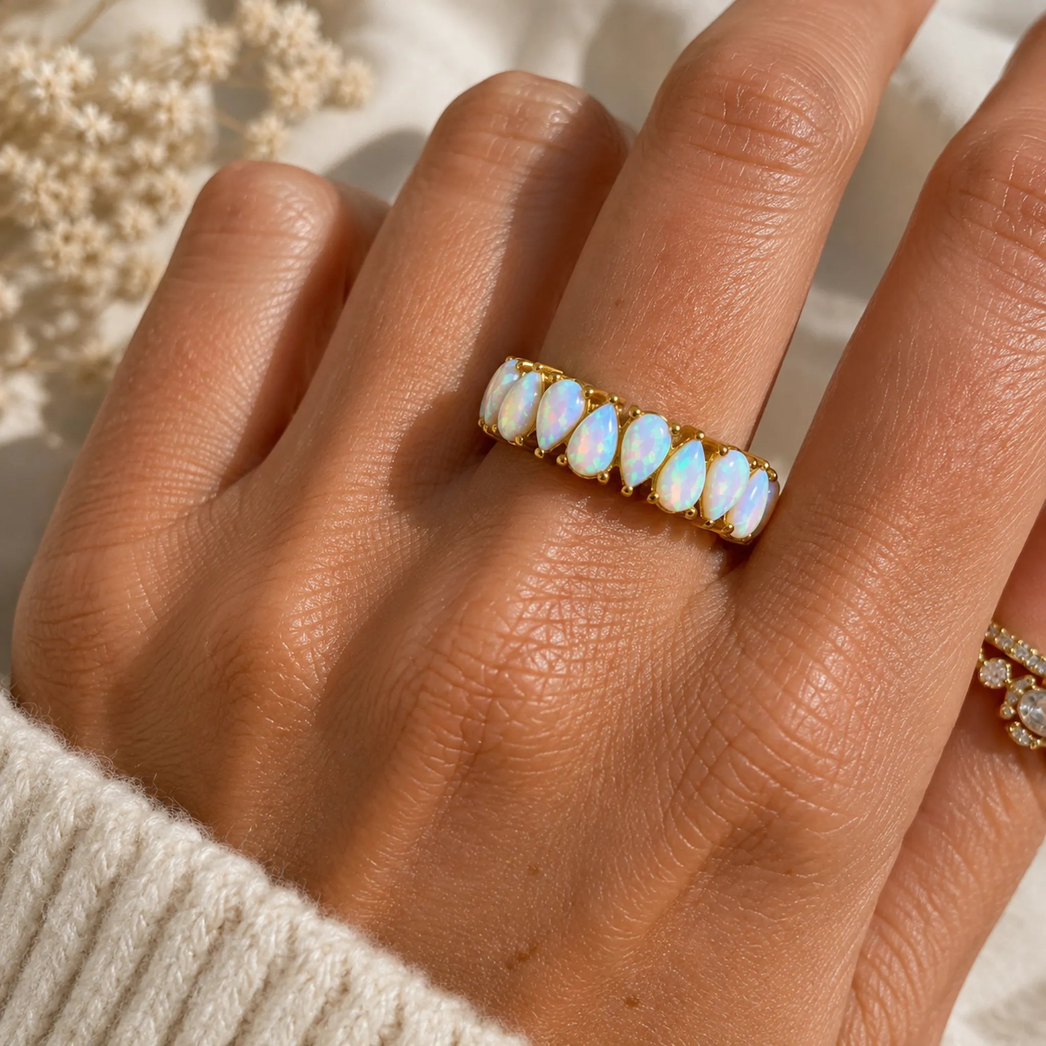 A gold white opal band ring featuring a row of teardrop-shaped lab grown white opal stones, worn on a hand.