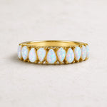 A gold eternity ring featuring a row of teardrop-shaped white opal gemstones, set against a neutral light gray background.