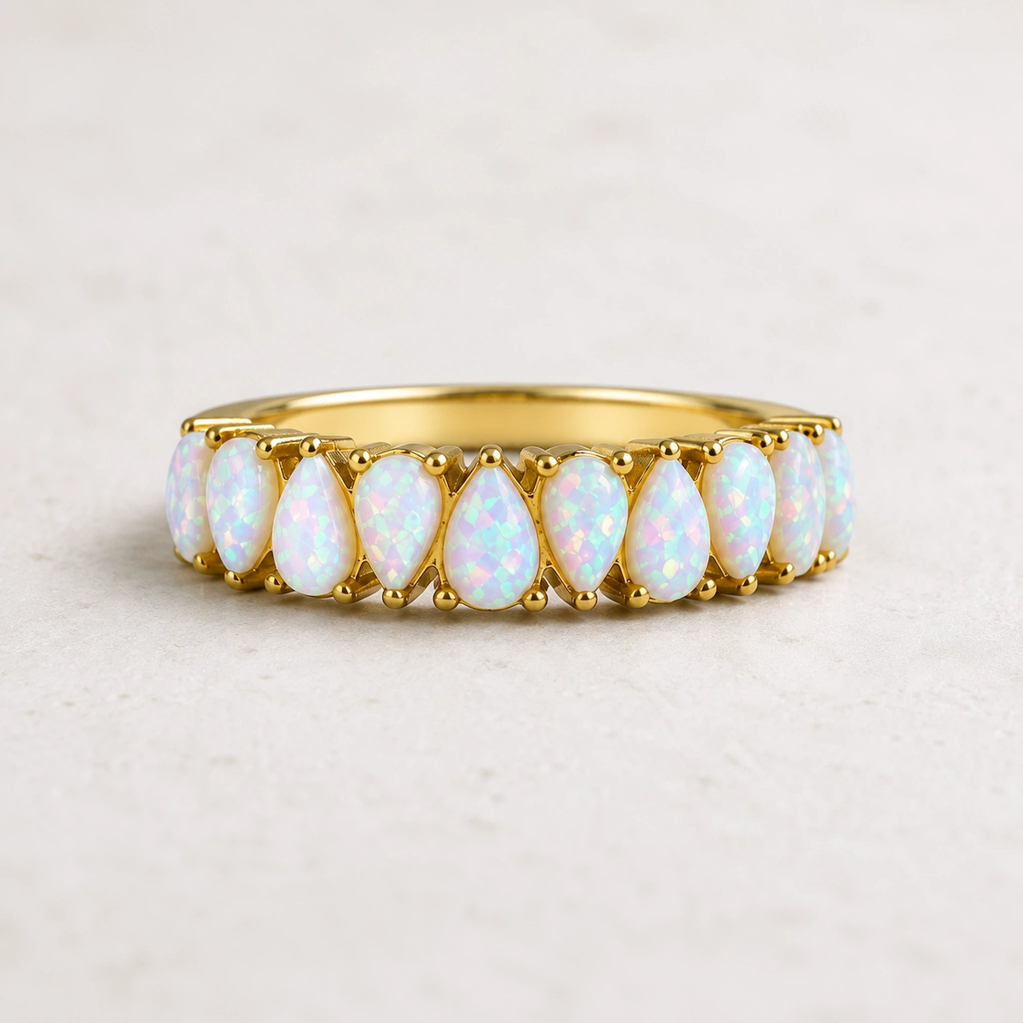 A gold white opal eternity ring featuring a row of teardrop-shaped lab-grown white opal gemstones, against light background.