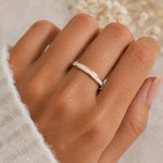 Hand wearing a gold ring with a stone on a neutral background