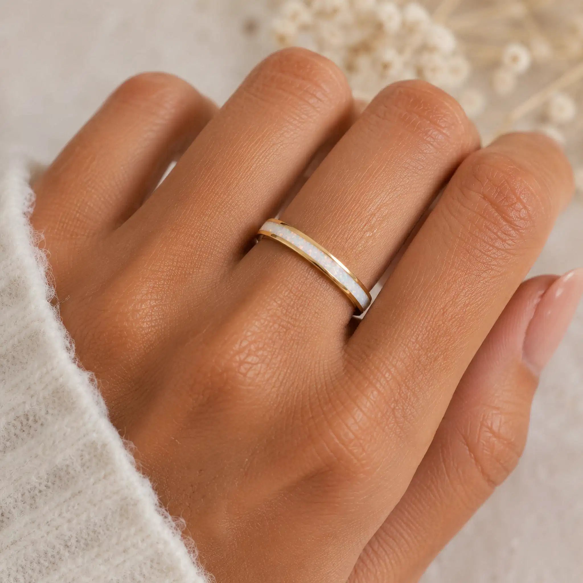 Hand wearing a gold ring with a stone on a neutral background